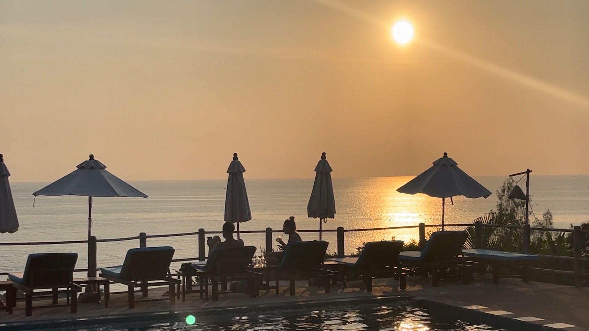 Sunset over a calm sea seen from a quiet resort terrace with parasols and loungers
